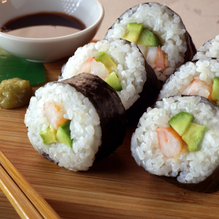 Maki rolls filled with shrimp and avocado on a bamboo board with soy sauce and wasabi