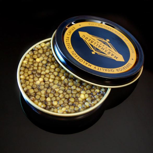 Open tin of golden Osetra caviar beside a navy lid reading Marshallberg superior quality malossol