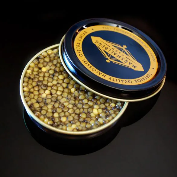Open tin of golden Osetra caviar beside a navy lid reading Marshallberg superior quality malossol