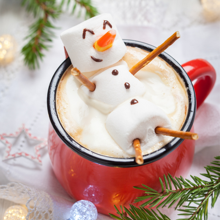 Red mug of hot chocolate topped with a marshmallow snowman with pretzel arms and a candy nose