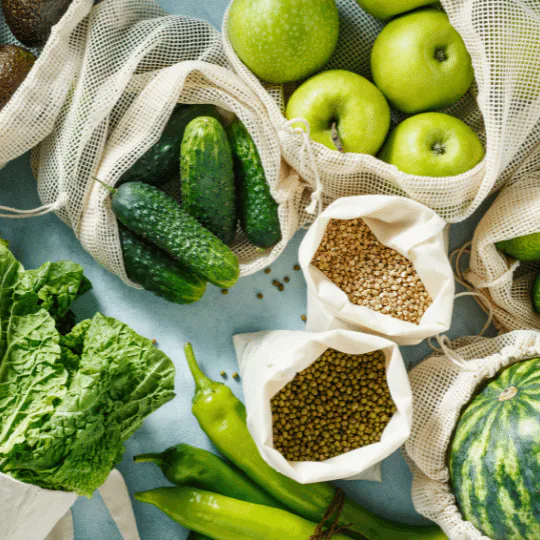 Mesh produce bags holding cucumbers, green apples, lentils and mung beans among fresh vegetables