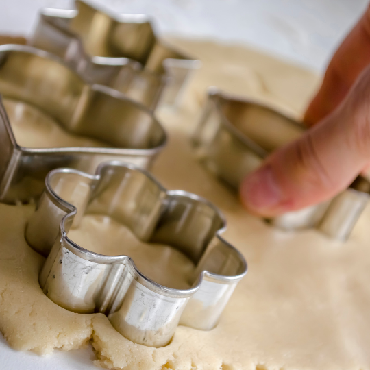 Hand pressing metal cookie cutters into rolled-out sugar cookie dough