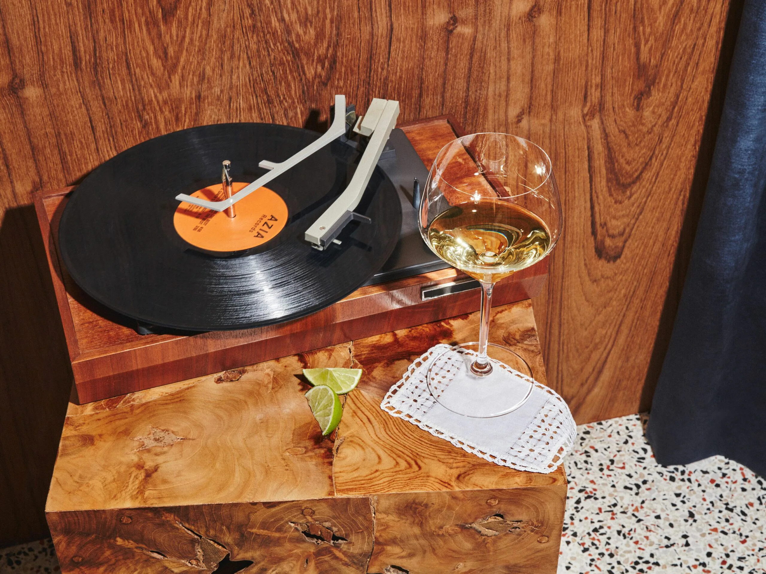 Pale gold Mexican Chardonnay cocktail in a stemmed glass beside a vinyl record player and a lime wedge