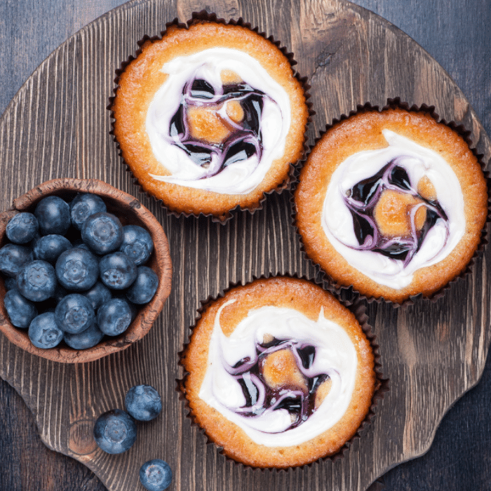Three mini cheesecake bites with blueberry swirl beside a bowl of fresh blueberries