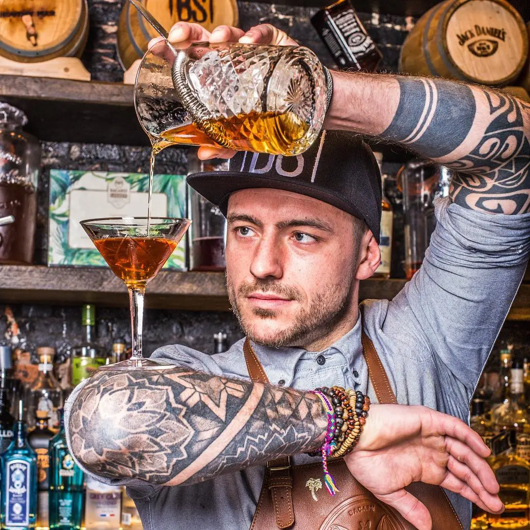 Mixologist Donald Simons straining an amber cocktail from a crystal mixing glass into a martini glass