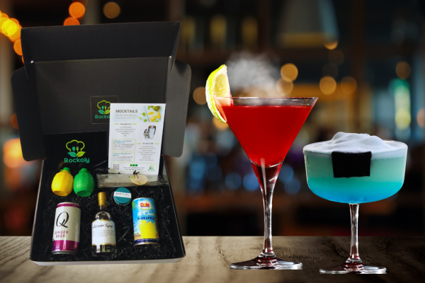 Cocktail kit box beside a blue cocktail topped with foam and nori and a smoking red drink with lemon