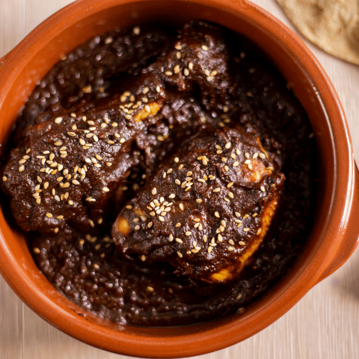 Chicken smothered in dark mole sauce and sprinkled with sesame seeds in a terracotta bowl