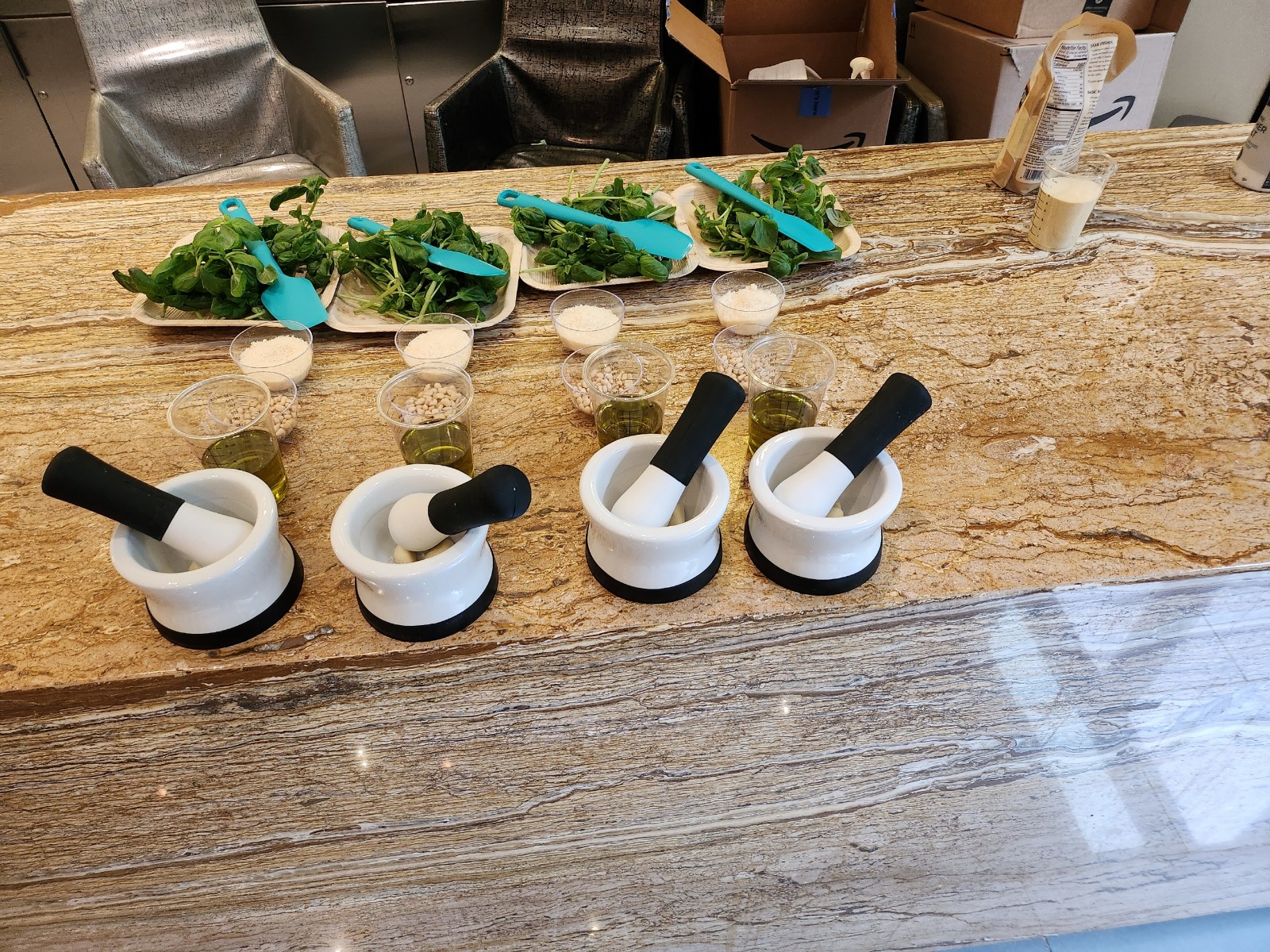 Row of white mortars and pestles with plates of fresh herbs and small glasses of green oil