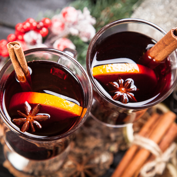 Two glasses of hot mulled wine topped with orange slices, star anise and cinnamon sticks, from above