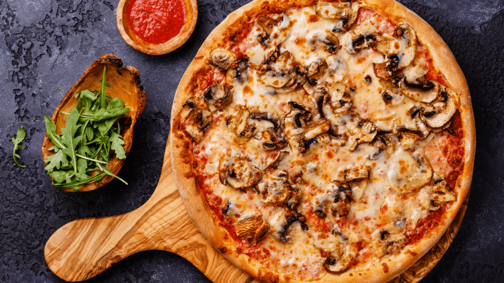 Overhead mushroom and mozzarella pizza on a wooden board with tomato sauce and fresh arugula
