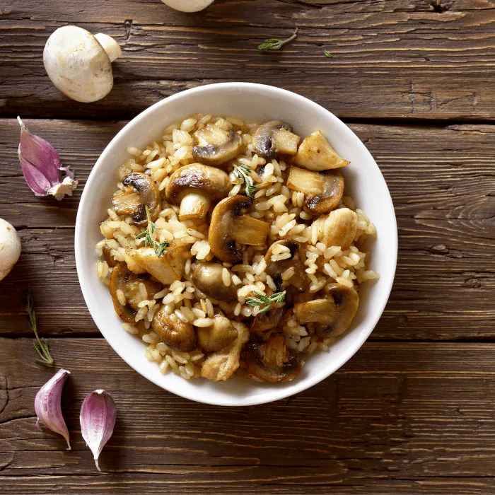 Overhead bowl of creamy mushroom risotto with thyme on a rustic wooden table with garlic and mushrooms