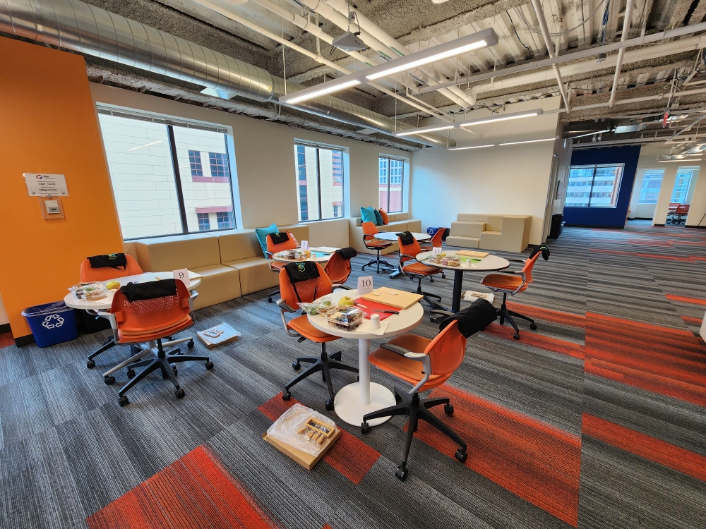 Office breakout lounge with orange chairs and round tables set with food for an in-person event