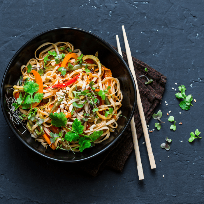 Bowl of stir-fried rice noodles with carrot, bean sprouts and cilantro, chopsticks alongside