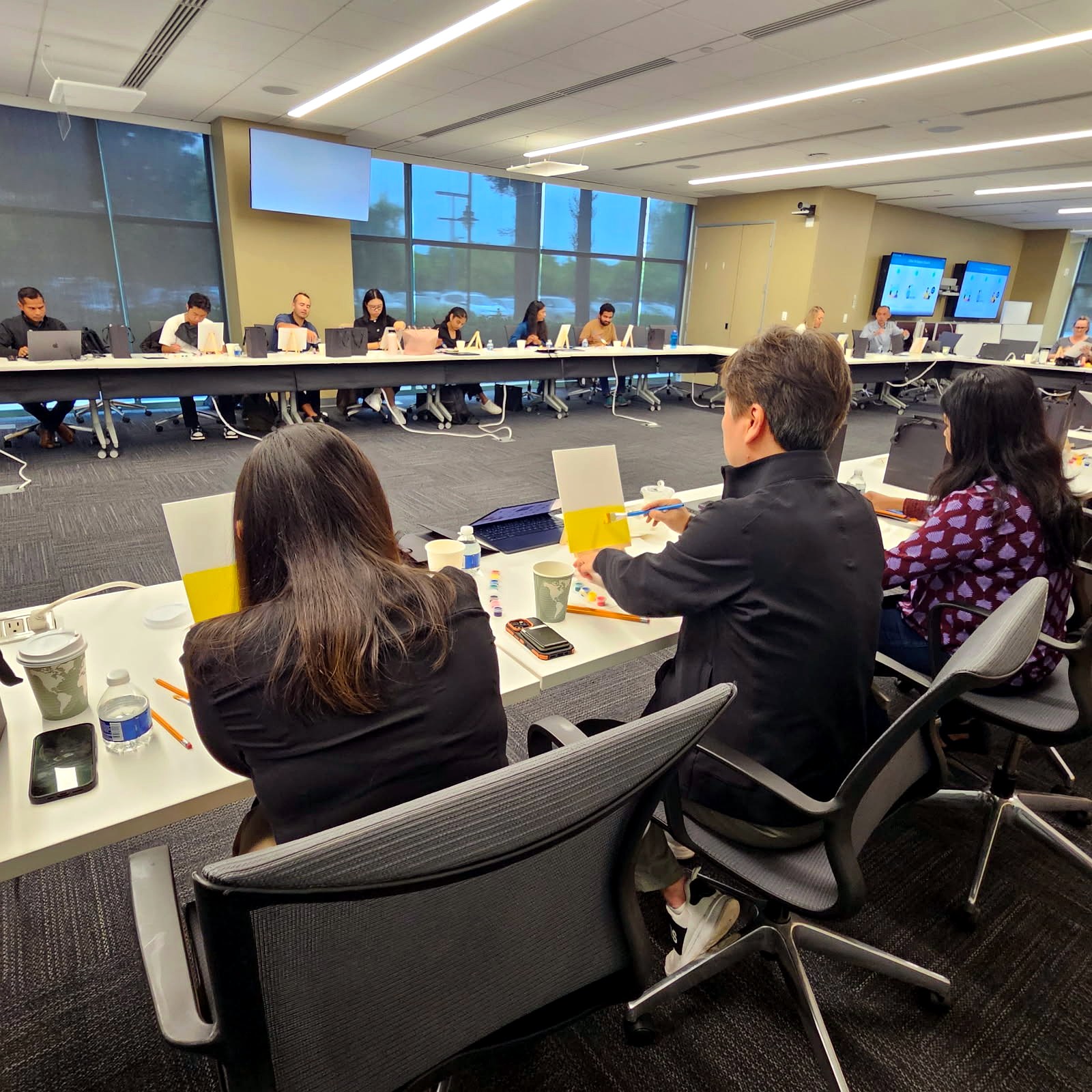 Employees painting at their seats around a large conference room table with canvases and supplies