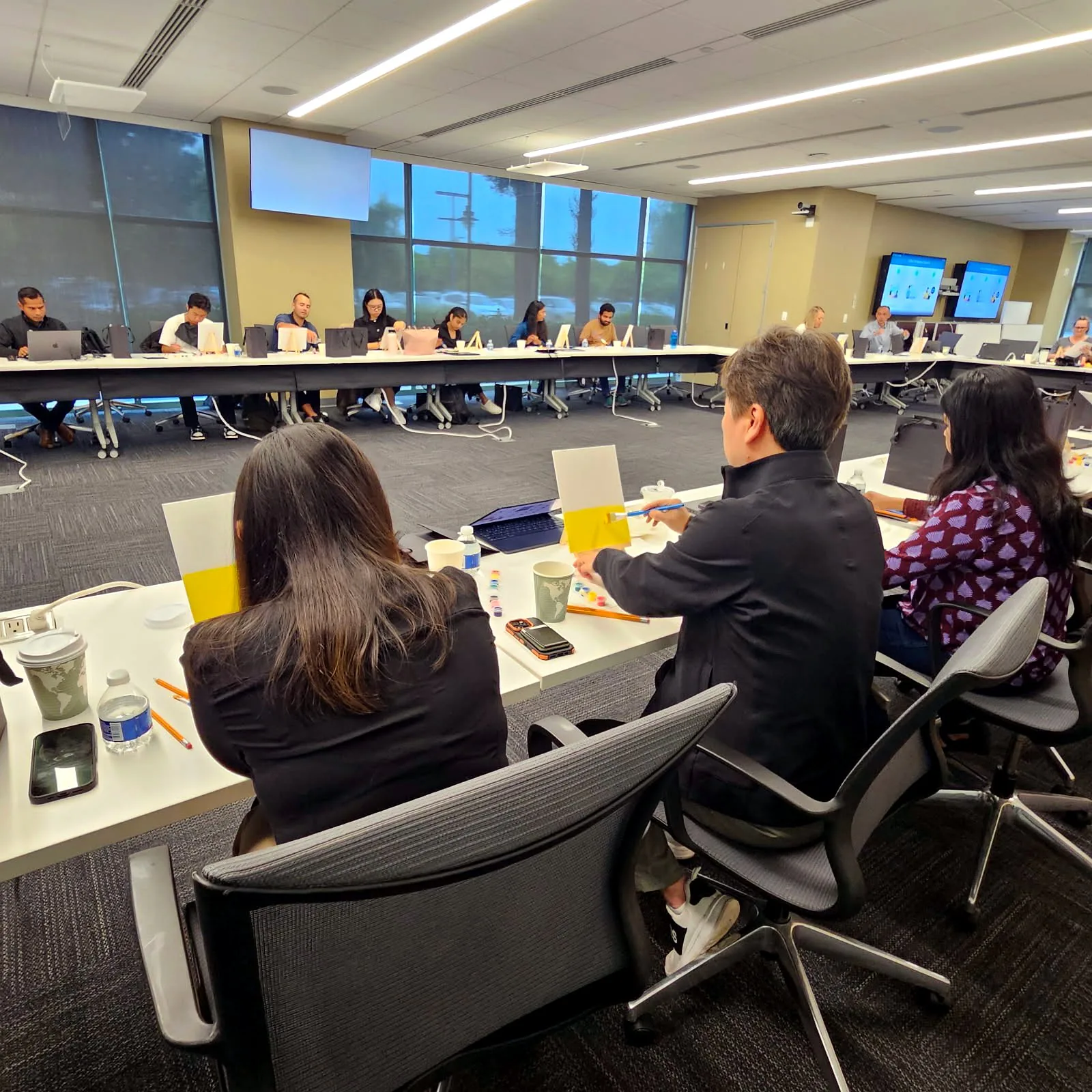 Employees painting at their seats around a large conference room table with canvases and supplies
