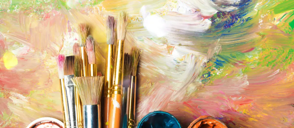 Bunch of paintbrushes standing against a swirl of multicoloured oil paint