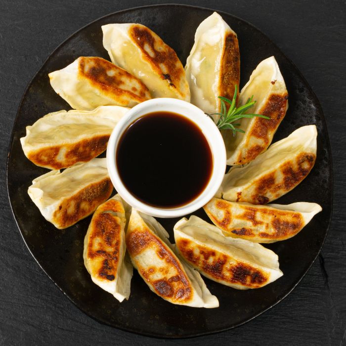 Pan-fried gyoza dumplings arranged in a ring around a bowl of dark soy dipping sauce