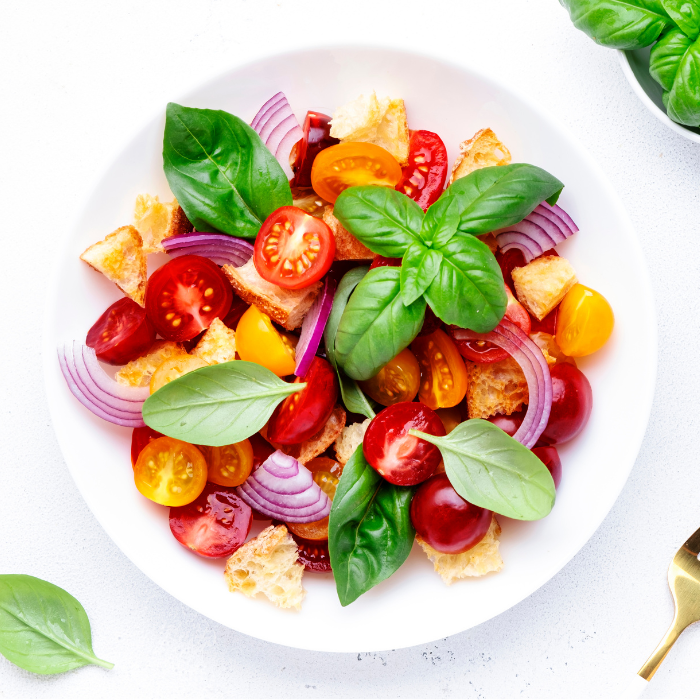 Overhead bowl of panzanella with cherry tomatoes, bread cubes, red onion and fresh basil