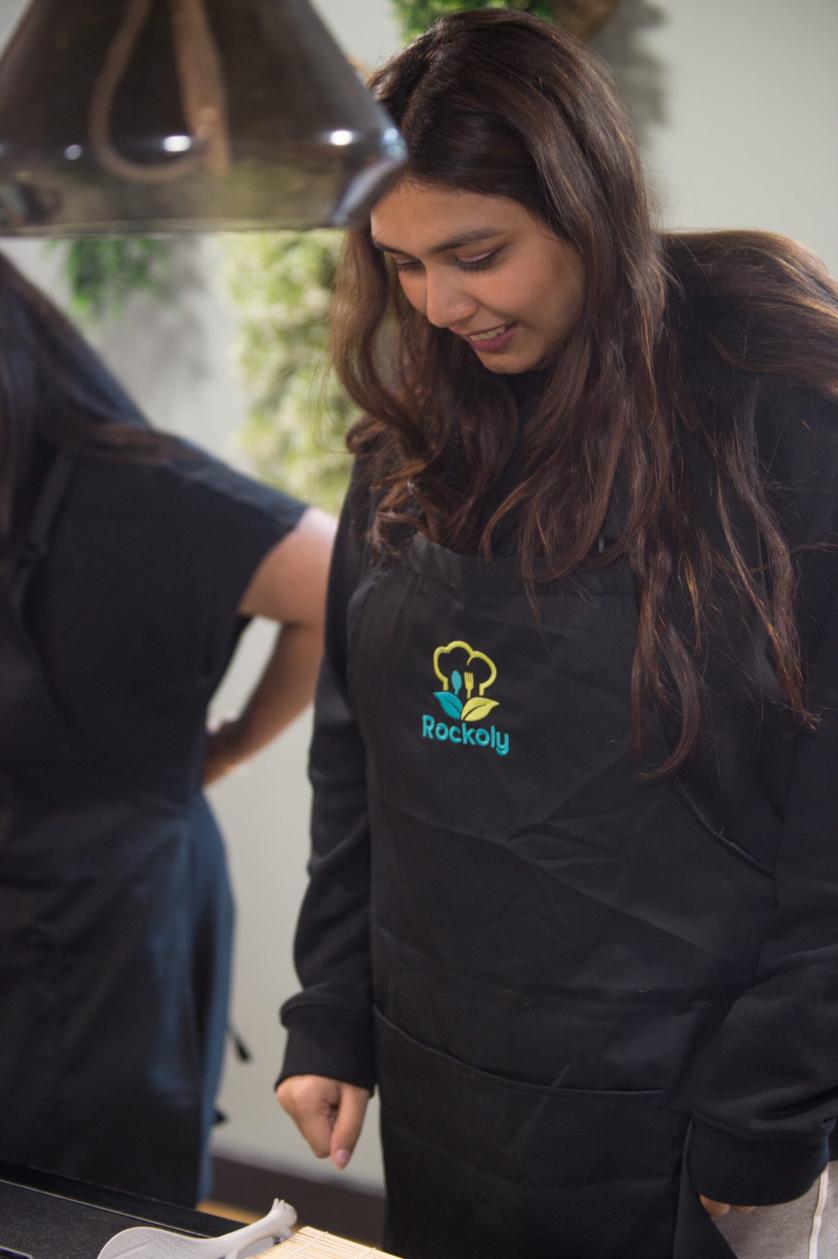 Participant in a black apron smiling as she works at her cooking station