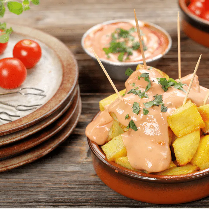 Terracotta dish of patatas bravas topped with creamy brava sauce, parsley and cocktail sticks