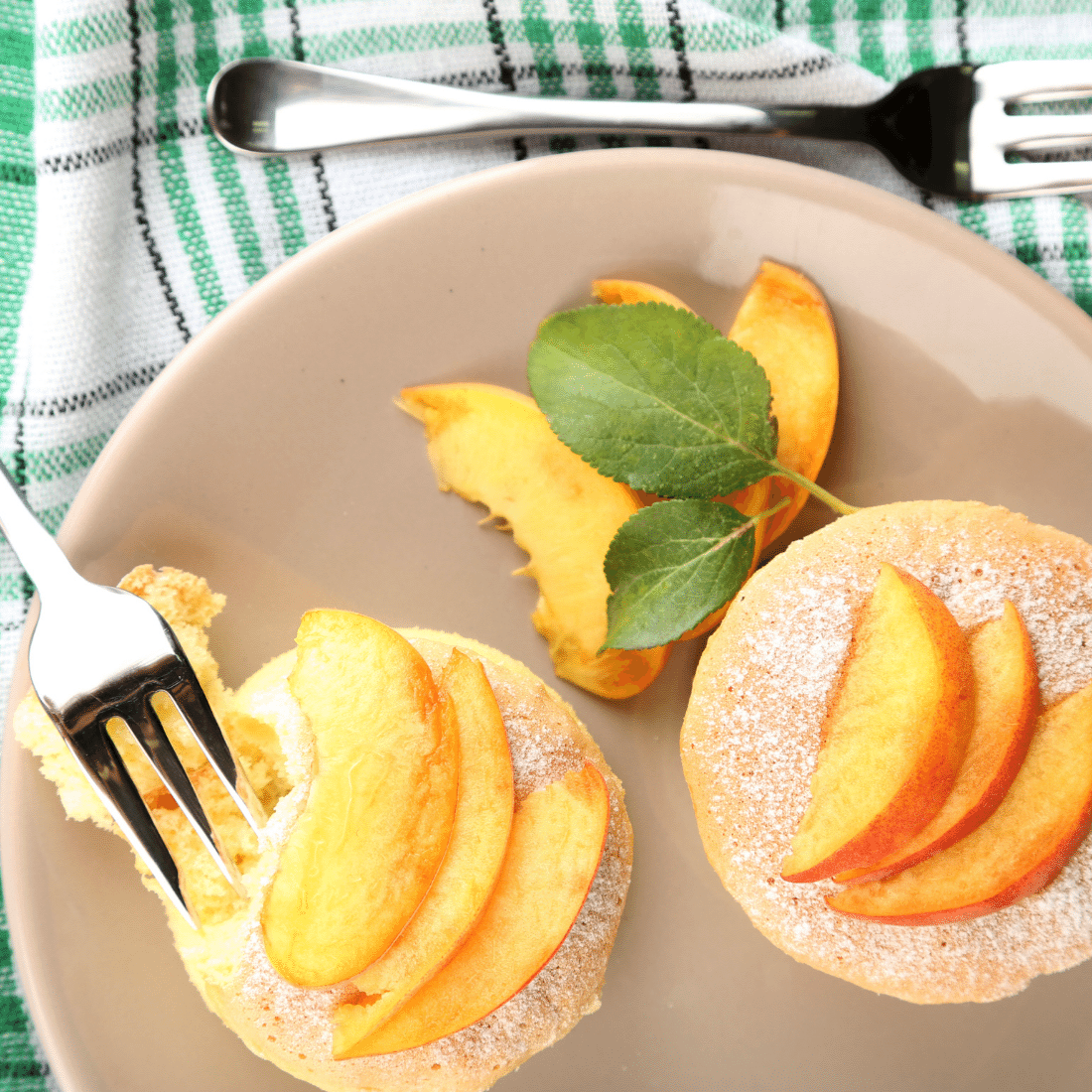 Small round tea cakes topped with fresh peach slices and powdered sugar, with a forkful lifted away