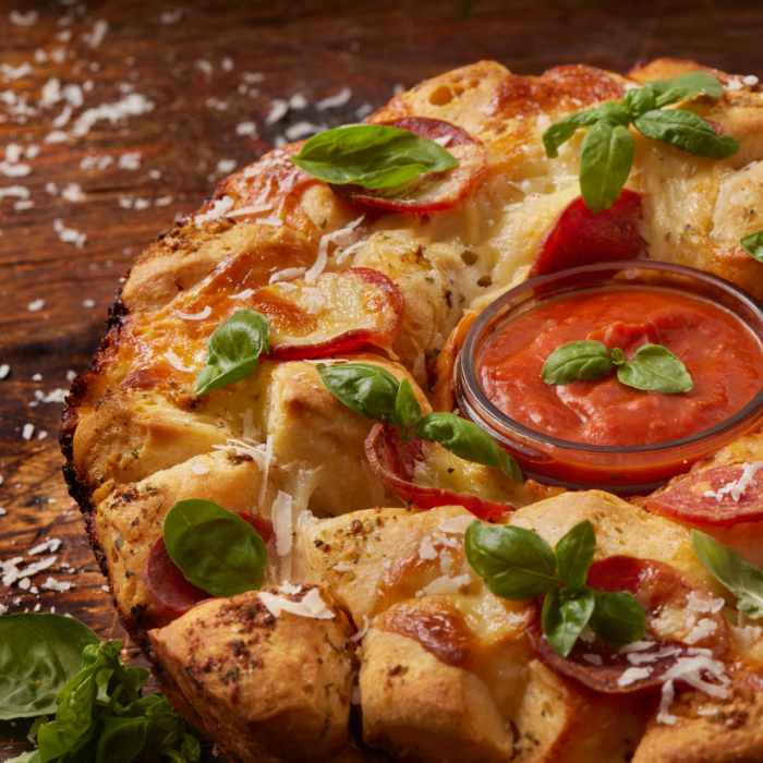 Pull-apart pepperoni pizza wreath topped with basil, with a bowl of marinara in the center