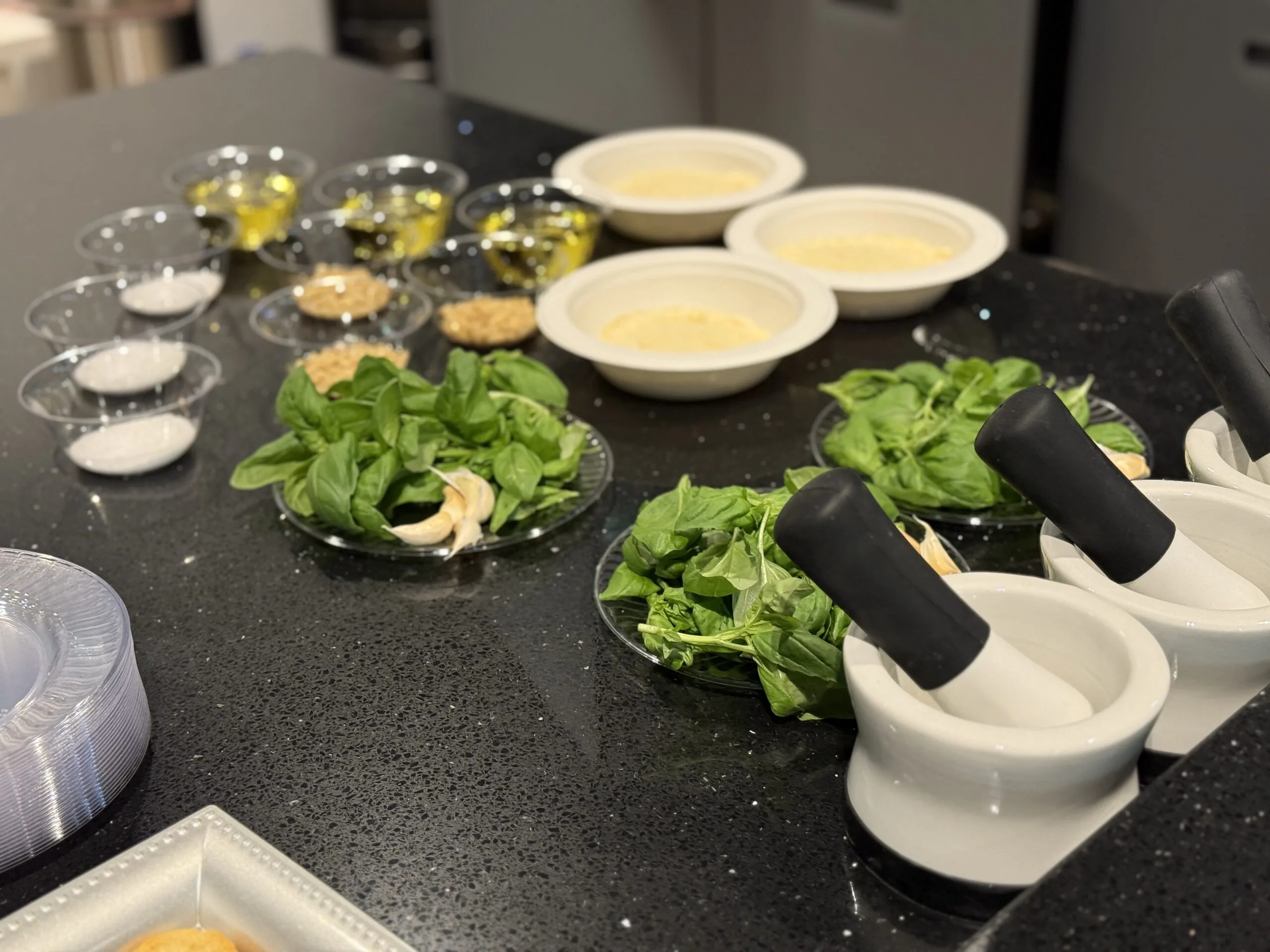 Prep station with mortars and pestles, fresh basil, garlic, olive oil and grated cheese portioned out