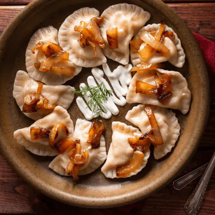 Cheese and potato pierogi on a stoneware plate under caramelized onion, with sour cream and dill