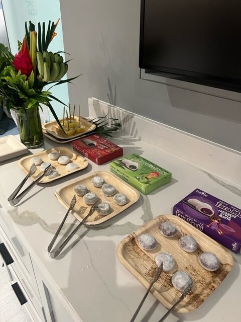 Wooden trays of powdered sugar dessert bites with serving tongs, beside tea boxes and flowers