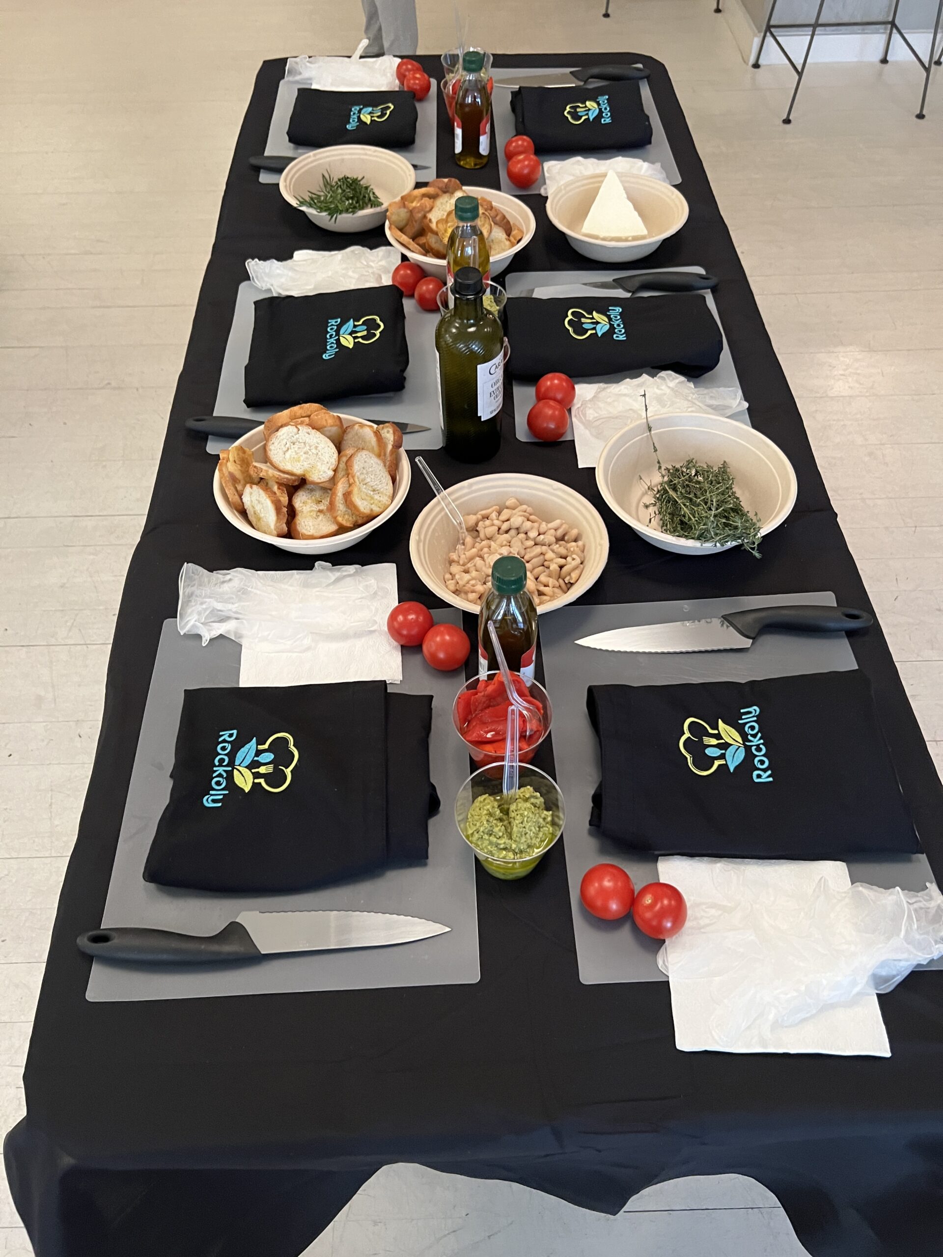 Prep station laid out with folded aprons, chef knives, bread, chickpeas, tomatoes and olive oil