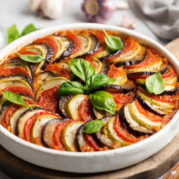 Ratatouille of thinly sliced zucchini, eggplant and tomato layered in a round dish with basil