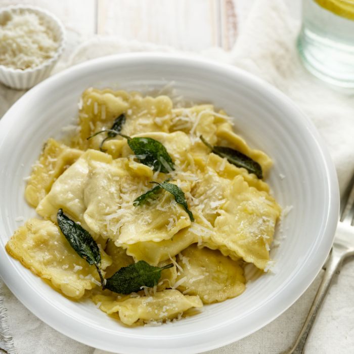 Bowl of ravioli tossed in brown butter with crisp sage leaves and grated Parmesan