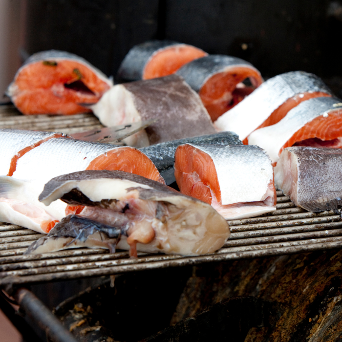Cut salmon fillets and steaks laid out on a smoker grate above smoldering wood