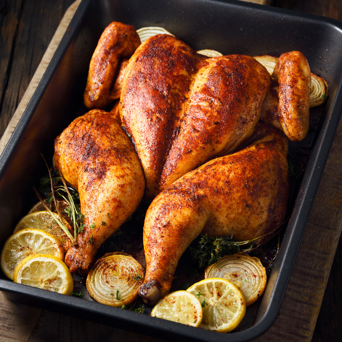 Golden roasted chicken in a black pan with lemon slices, onions and rosemary