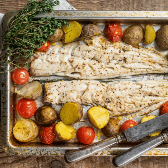 Two roasted white fish fillets on a sheet pan with baby potatoes, cherry tomatoes and thyme