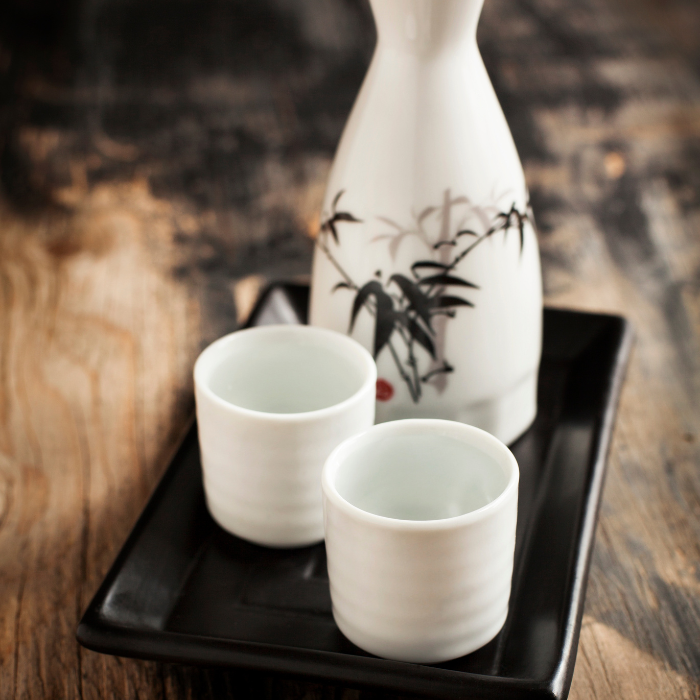 White ceramic sake bottle painted with bamboo and two small cups on a black lacquer tray