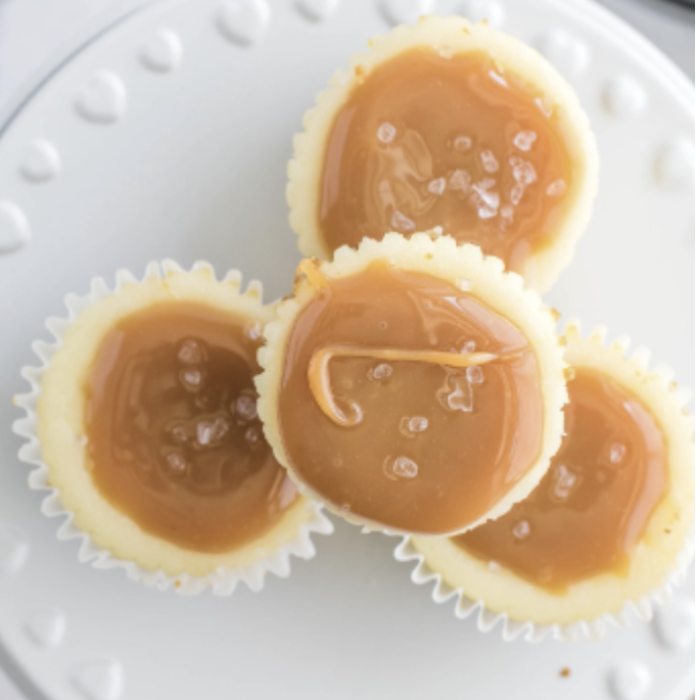 Three mini cheesecake bites topped with salted caramel and flaky sea salt on a white plate