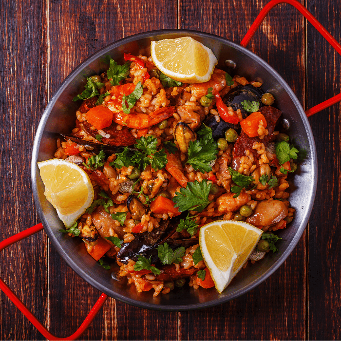 Paella pan of rice with shrimp, tomatoes, parsley and lemon wedges