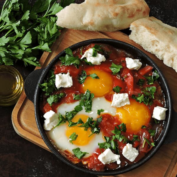 Shakshuka of eggs poached in spiced tomato sauce with feta and parsley, served with torn pita