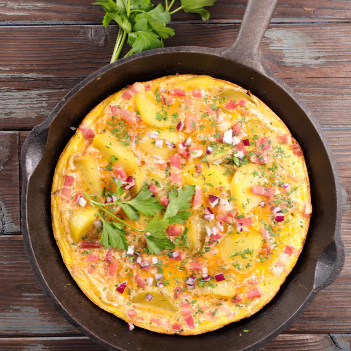 Open-faced skillet omelet with sliced potatoes, diced ham and parsley in a cast-iron pan