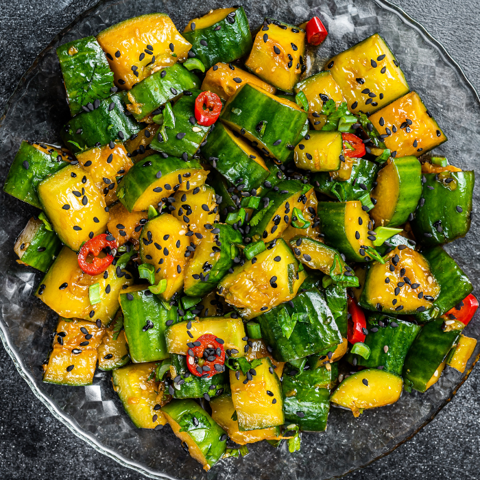 Chunks of smashed cucumber tossed with sesame seeds, scallions and red chili on a dark plate