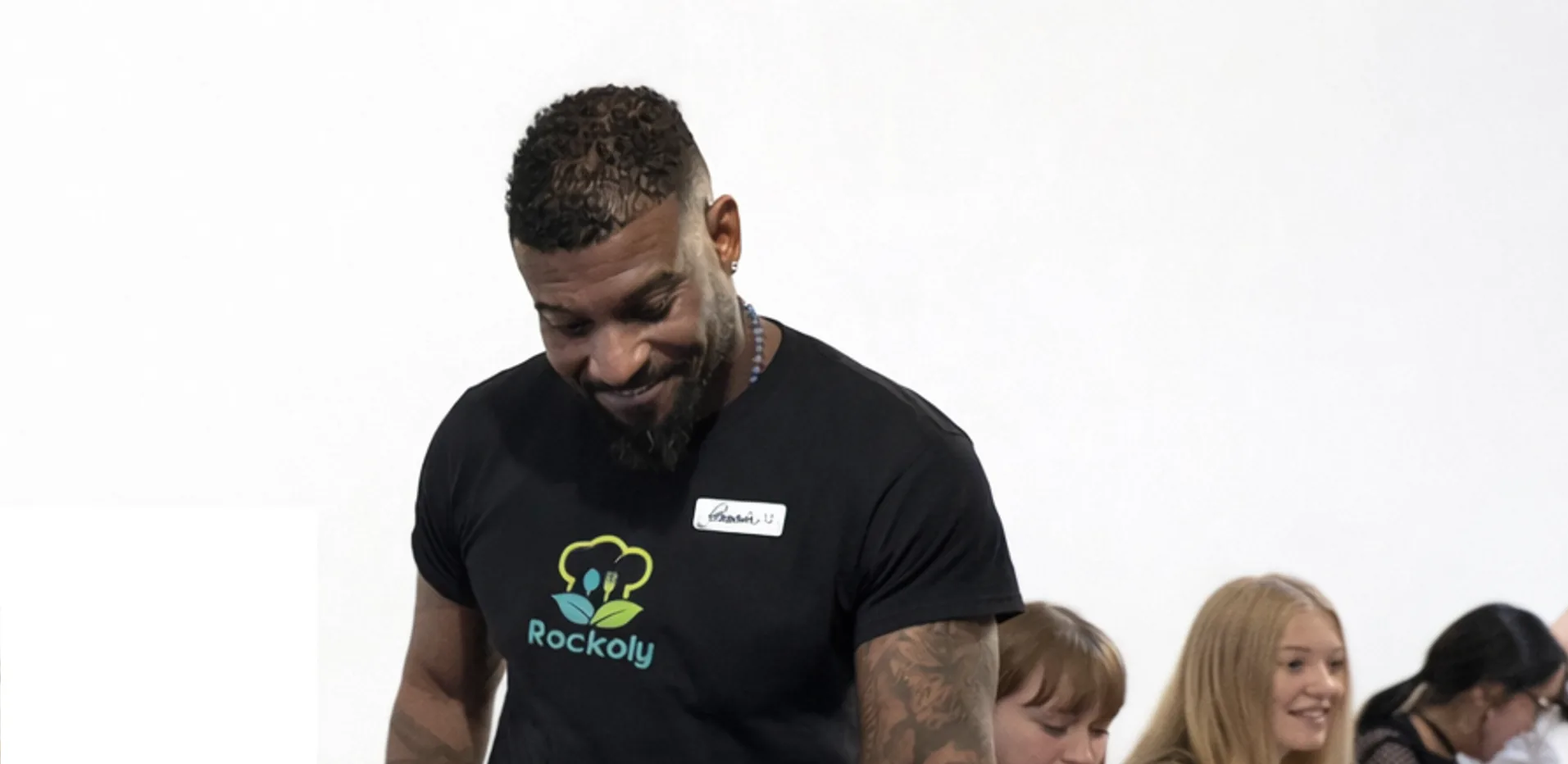 Smiling host in a black Rockoly T-shirt and name tag standing beside seated guests