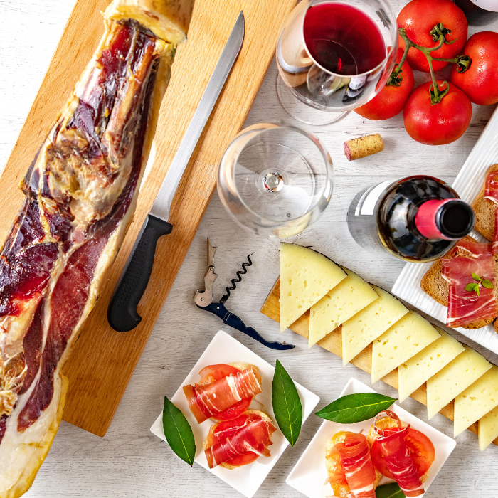 Spanish tapas spread with a leg of cured jamón on a carving board, sliced cheese, tomatoes and red wine
