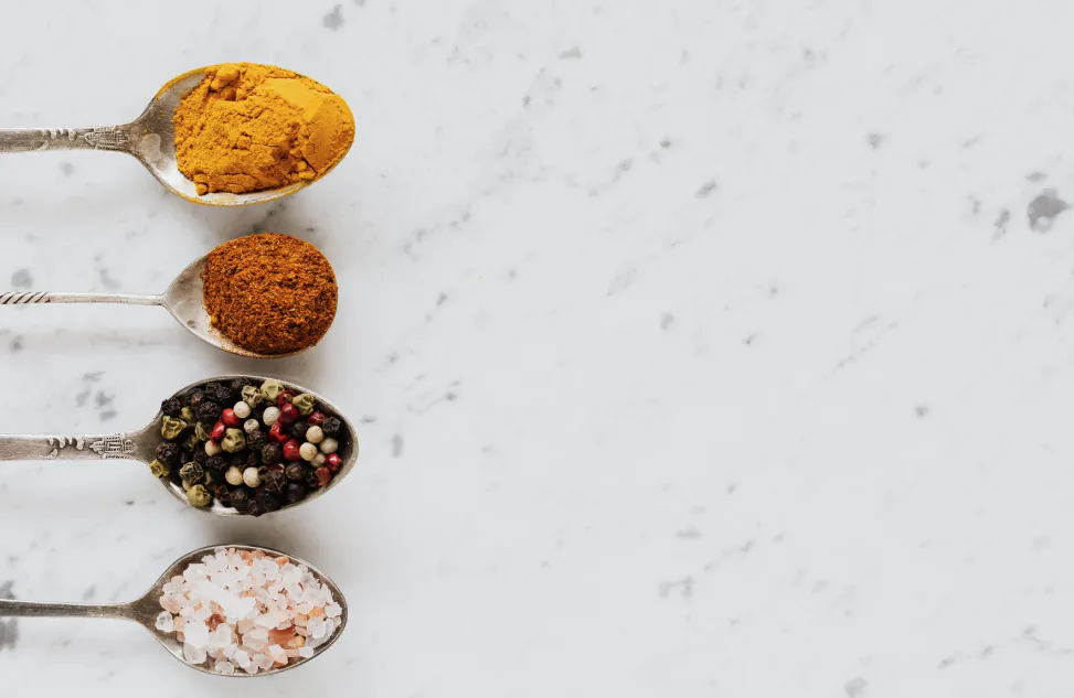 Four vintage spoons on white marble holding turmeric, paprika, mixed peppercorns and pink salt