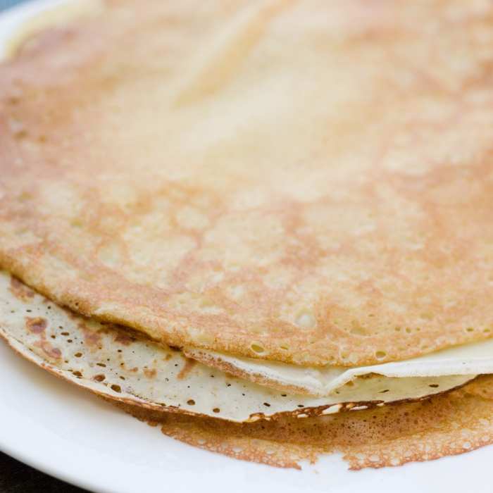 Stack of thin golden French crepes on a white plate