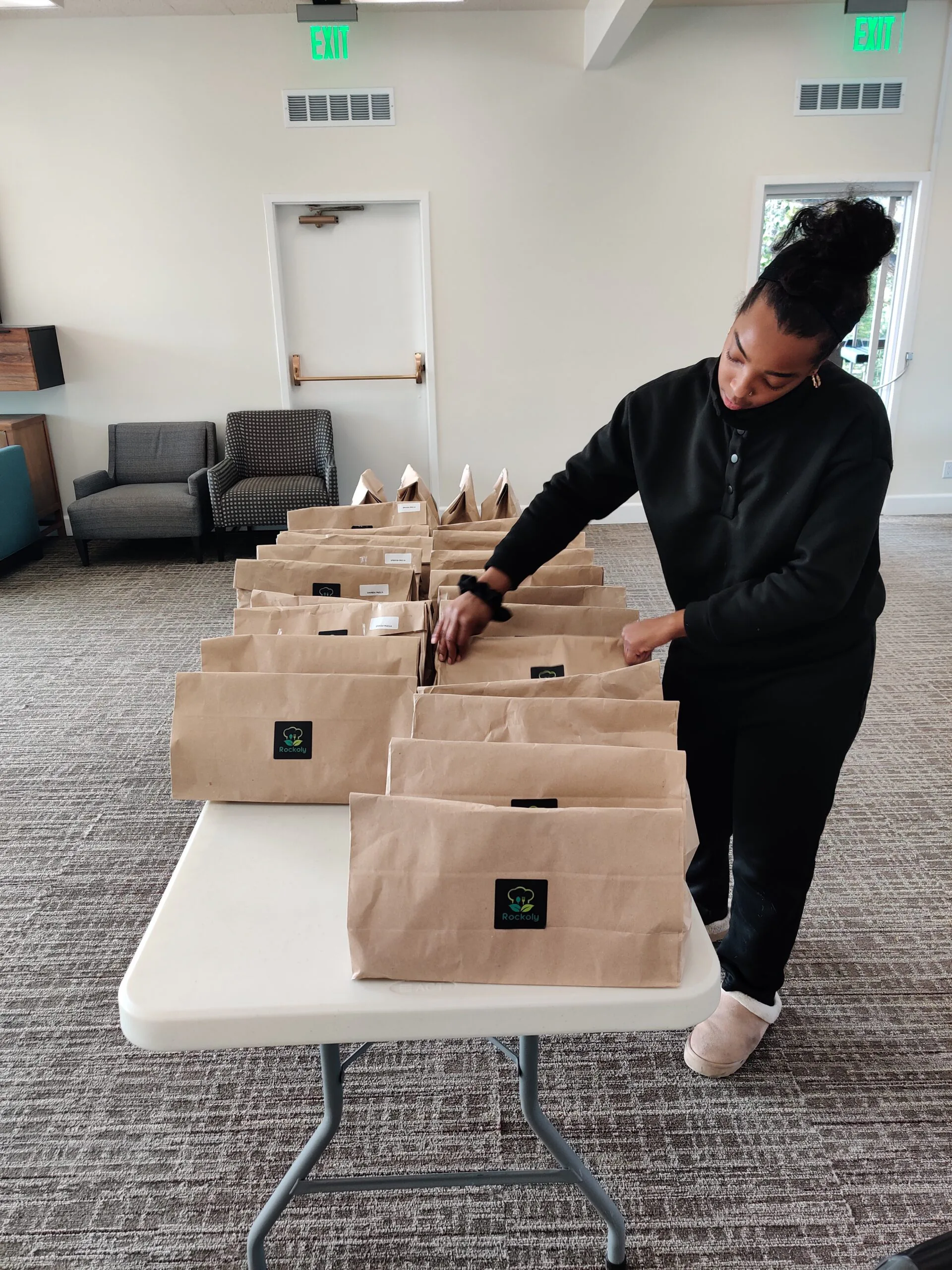 Woman lining up rows of brown paper event kit bags on a folding table in a community room