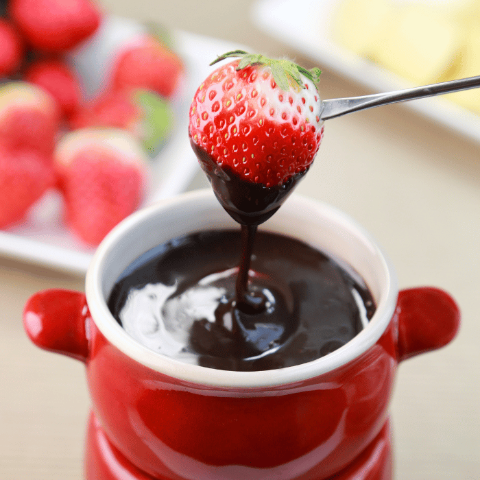 Strawberry on a fork dipped into a red pot of melted dark chocolate fondue
