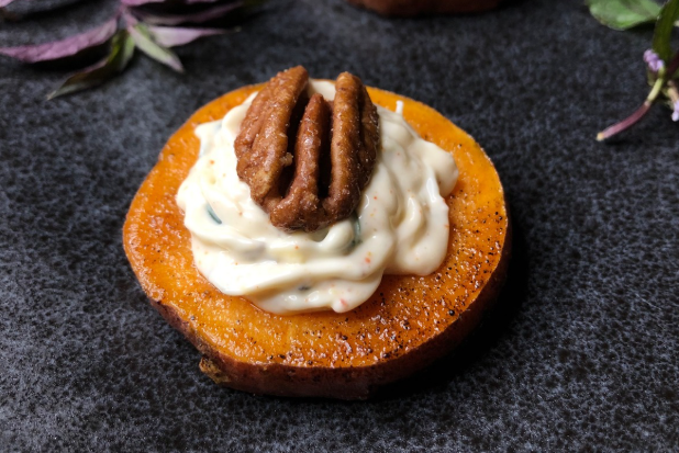 Roasted sweet potato round topped with a swirl of cream and a toasted pecan half