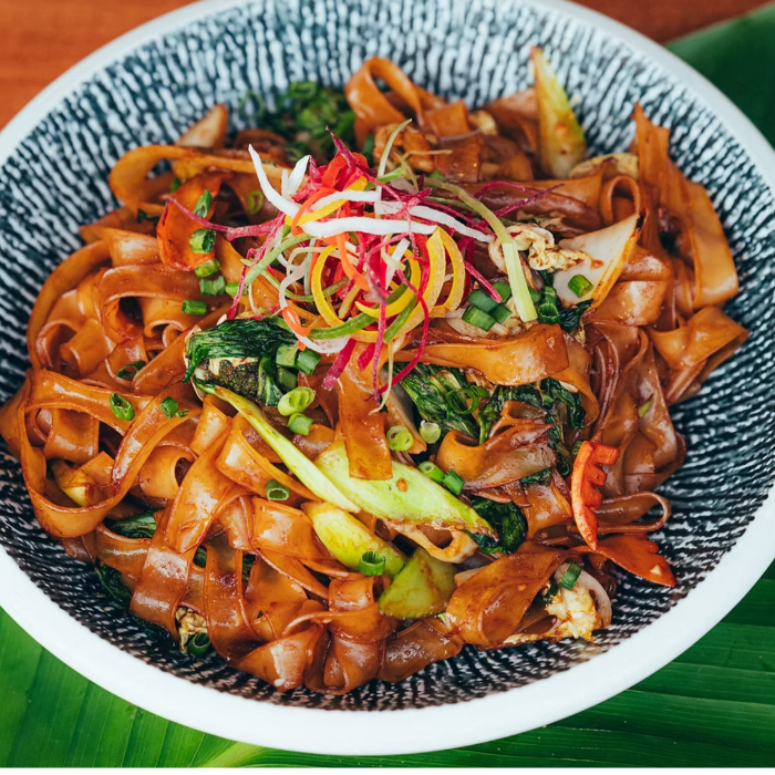 Bowl of wide rice noodles stir-fried with basil, scallions and chilies, topped with shredded vegetables
