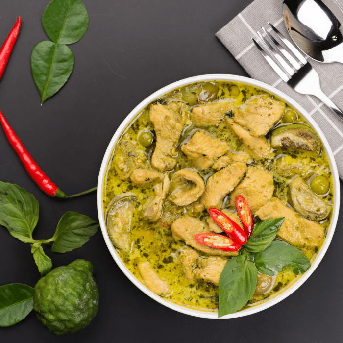Thai green coconut curry with chicken in a white bowl, topped with red chilies and Thai basil